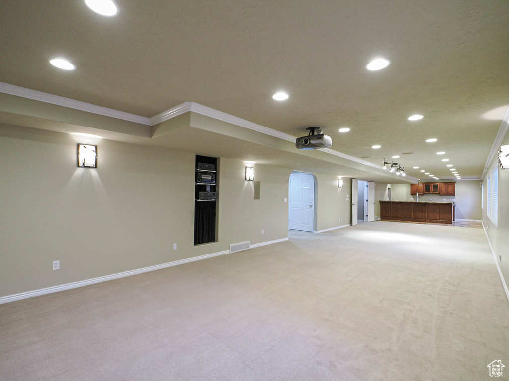 Unfurnished living room with crown molding, recessed lighting, light colored carpet, bar area, and arched walkways