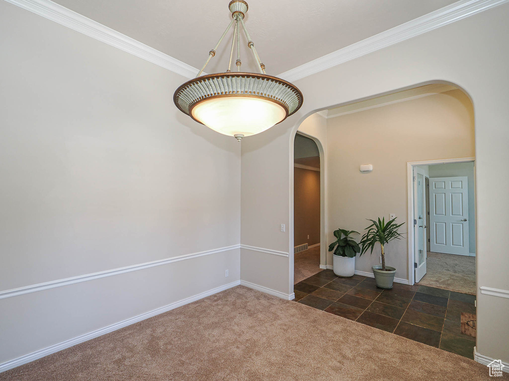 Tiled empty room with arched walkways, carpet floors, and crown molding