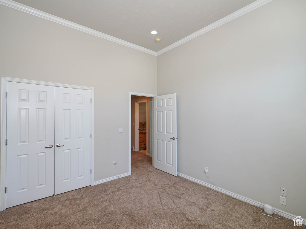 Unfurnished bedroom featuring carpet floors, crown molding, a closet, recessed lighting, and a high ceiling