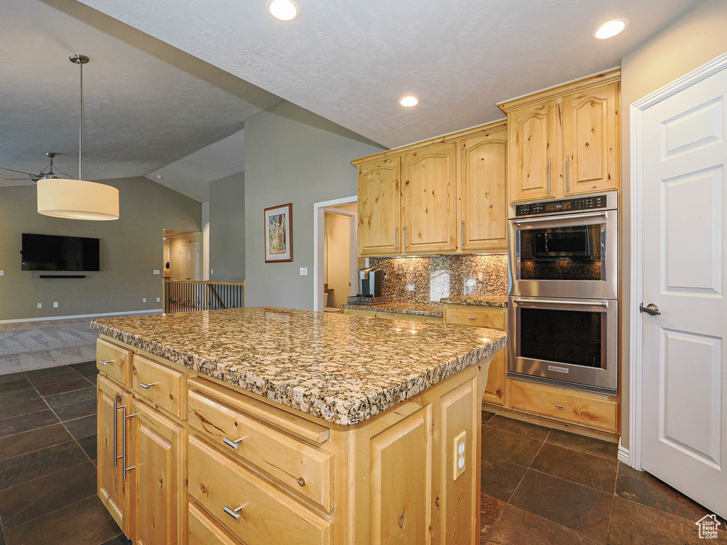 Kitchen with double oven, light brown cabinets, vaulted ceiling, a center island, and open floor plan