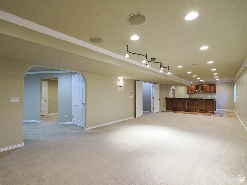 Unfurnished living room featuring arched walkways, ornamental molding, recessed lighting, light carpet, and bar