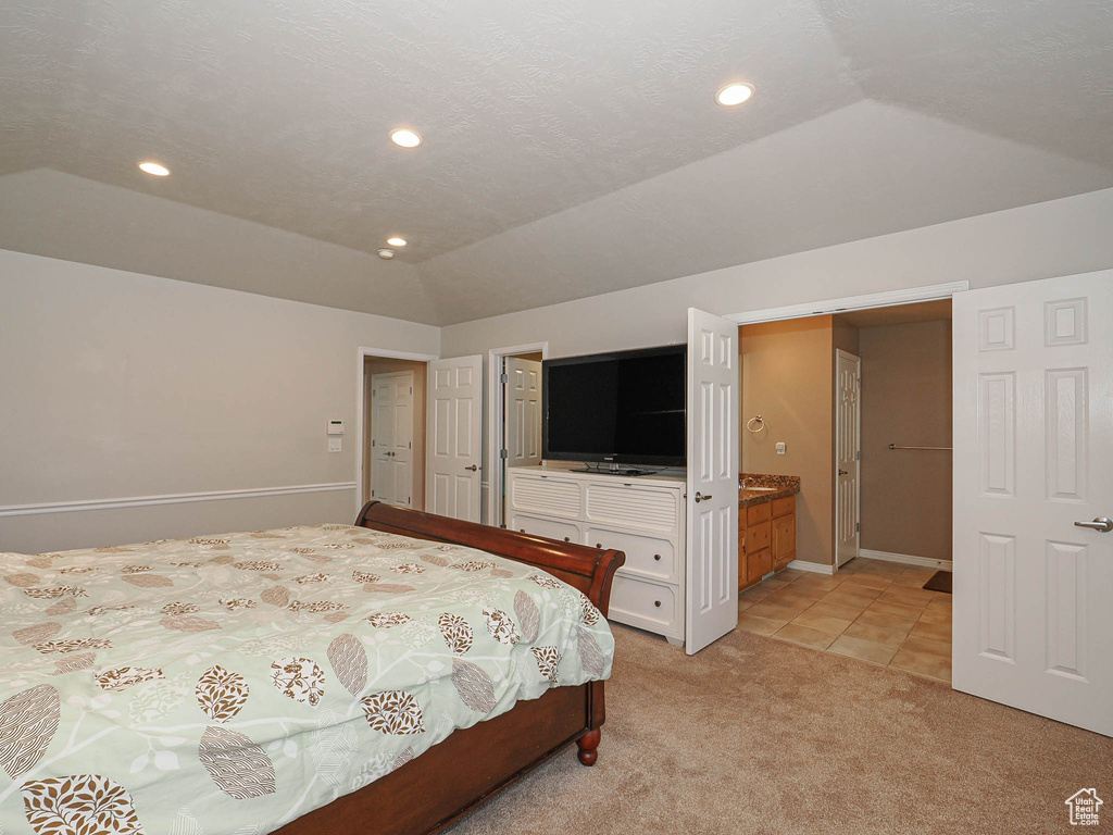 Bedroom with light colored carpet, recessed lighting, lofted ceiling, light tile patterned flooring, and ensuite bath