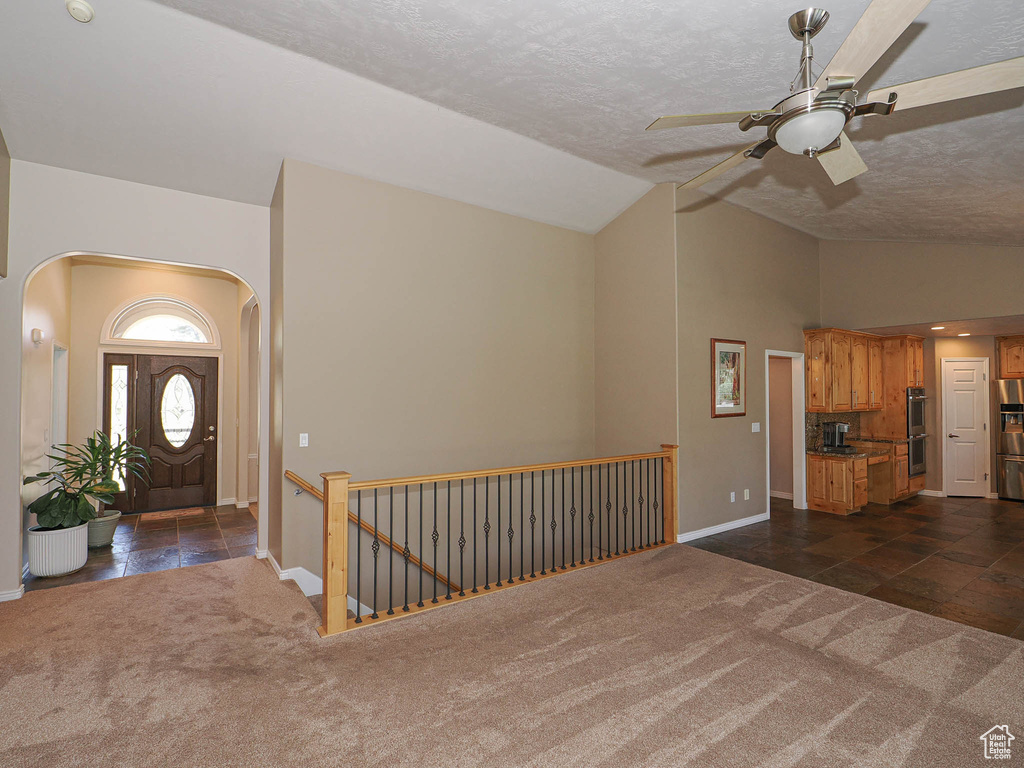Foyer entrance featuring arched walkways, vaulted ceiling, dark colored carpet, ceiling fan, and a textured ceiling