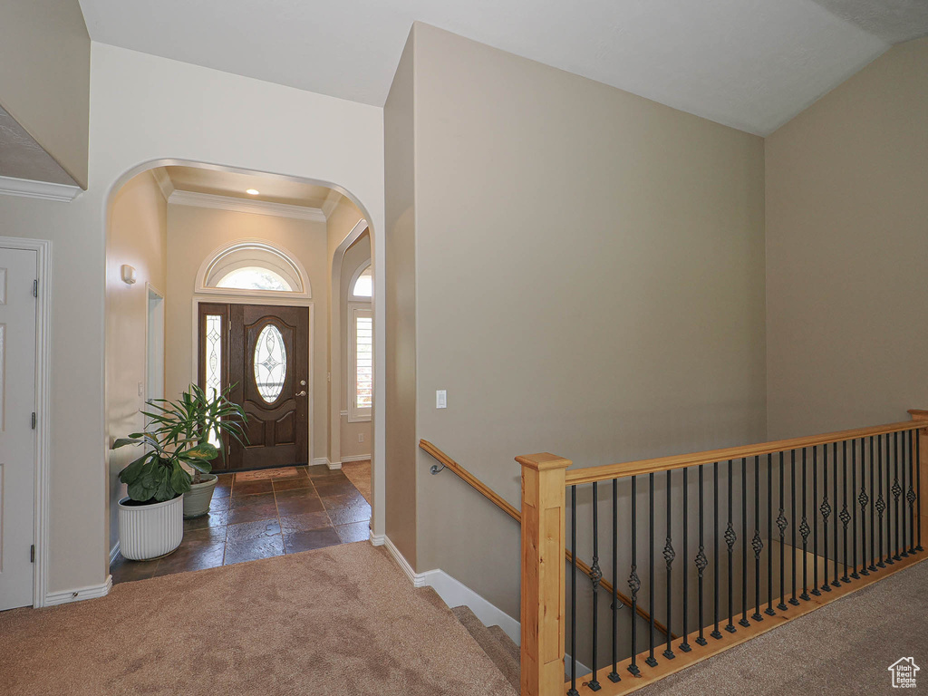 Carpeted entrance foyer featuring arched walkways, ornamental molding, and stone tile floors