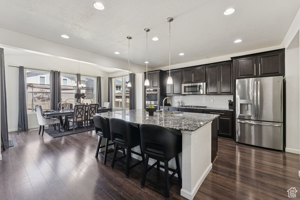 Kitchen featuring appliances with stainless steel finishes, an island with sink, recessed lighting, dark wood-type flooring, and a breakfast bar