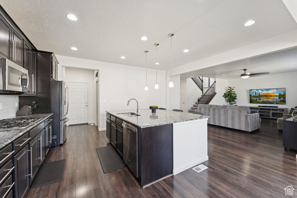 Kitchen featuring stainless steel appliances, open floor plan, a kitchen island with sink, dark wood finished floors, and recessed lighting