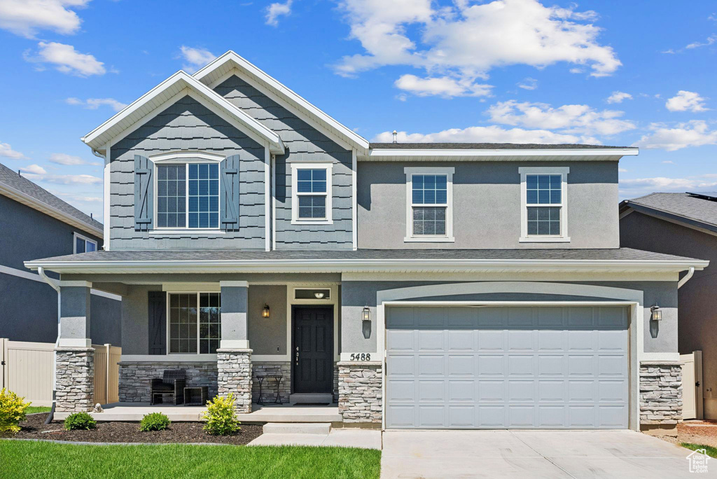 View of front of home featuring stone siding, a porch, concrete driveway, and an attached garage