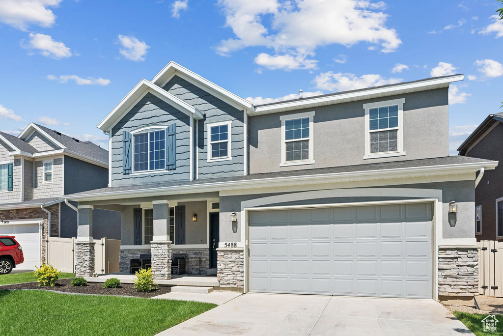 View of front facade with stone siding, covered porch, an attached garage, driveway, and stucco siding