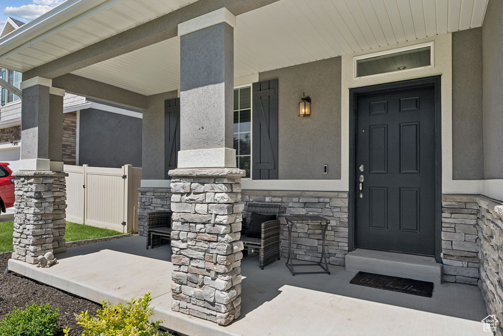 Doorway to property with stone siding, a porch, and stucco siding