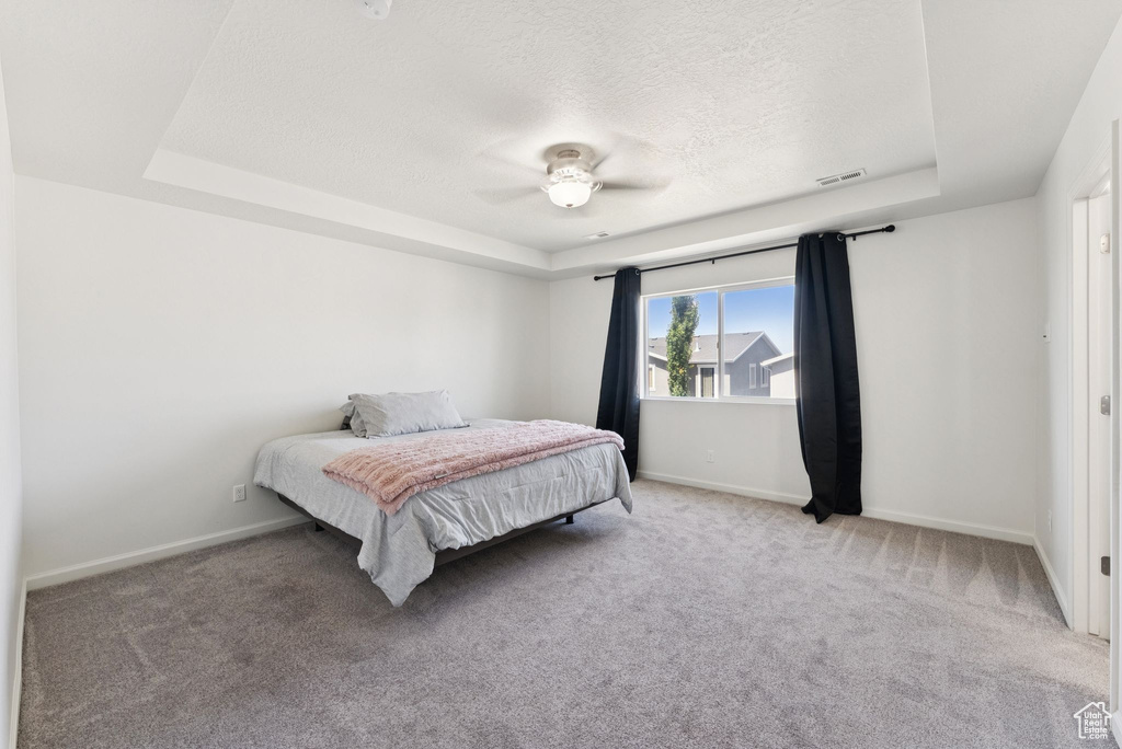 Carpeted bedroom featuring a tray ceiling, a textured ceiling, and a ceiling fan