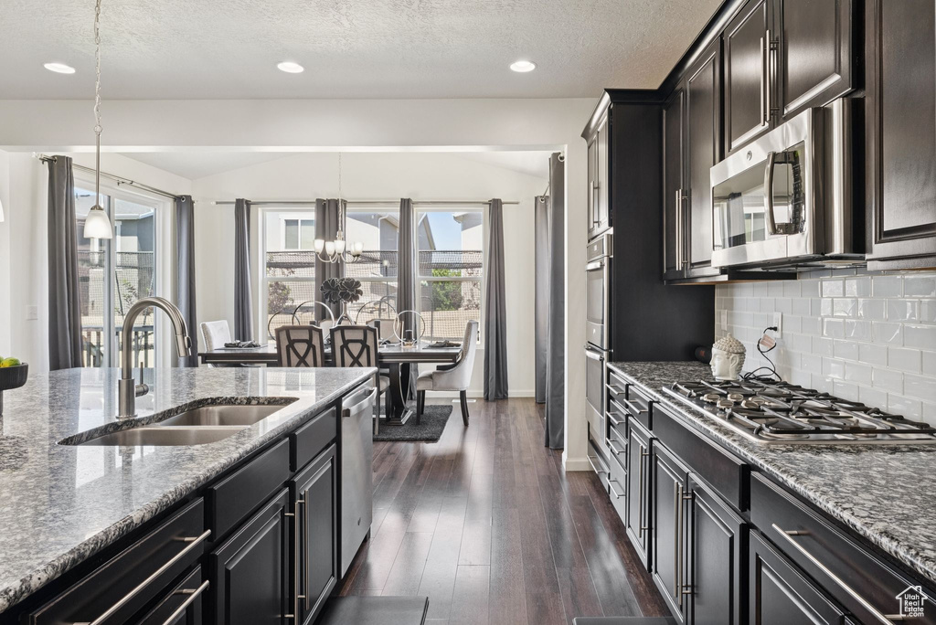 Kitchen featuring stainless steel appliances, stone counters, tasteful backsplash, dark wood-style flooring, and a textured ceiling