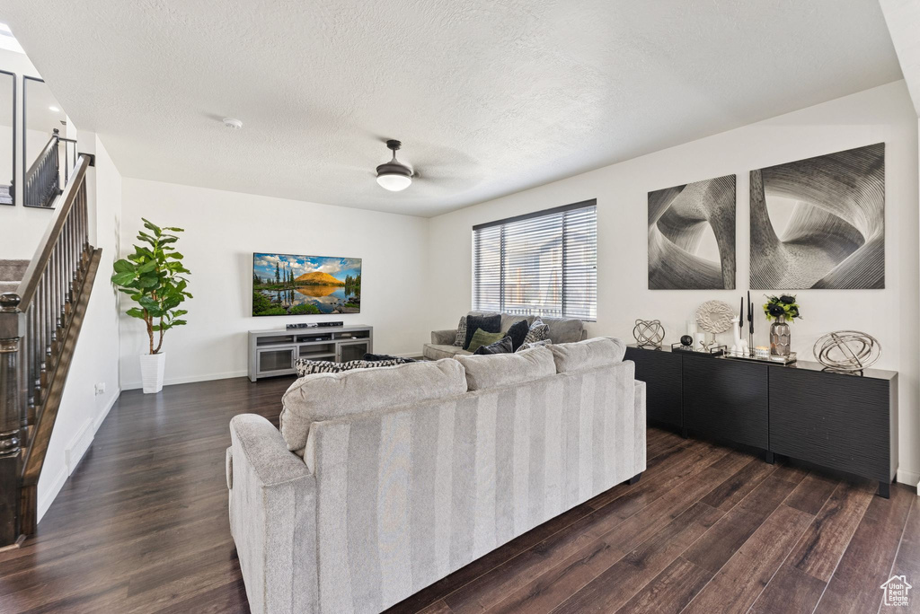 Living room with dark wood-style floors, stairs, a ceiling fan, and a textured ceiling