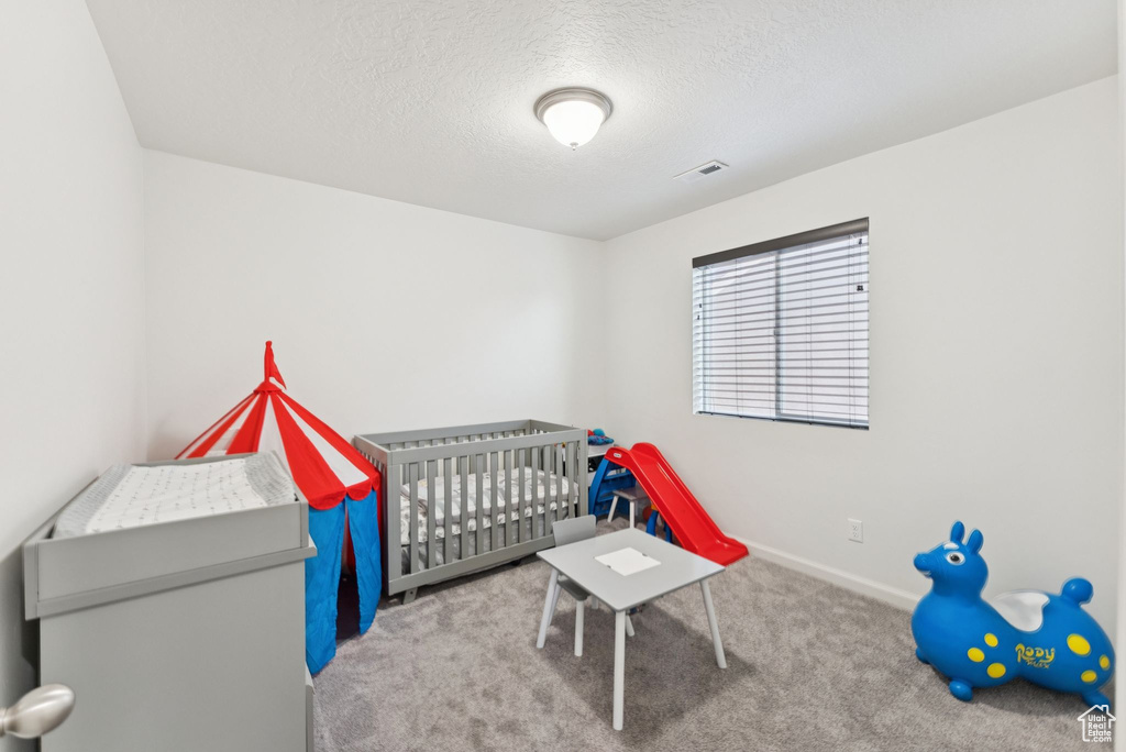 Bedroom with carpet, a textured ceiling, and a nursery area