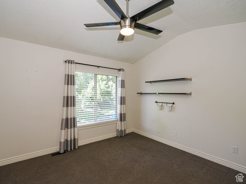 Spare room featuring lofted ceiling, ceiling fan, and dark colored carpet