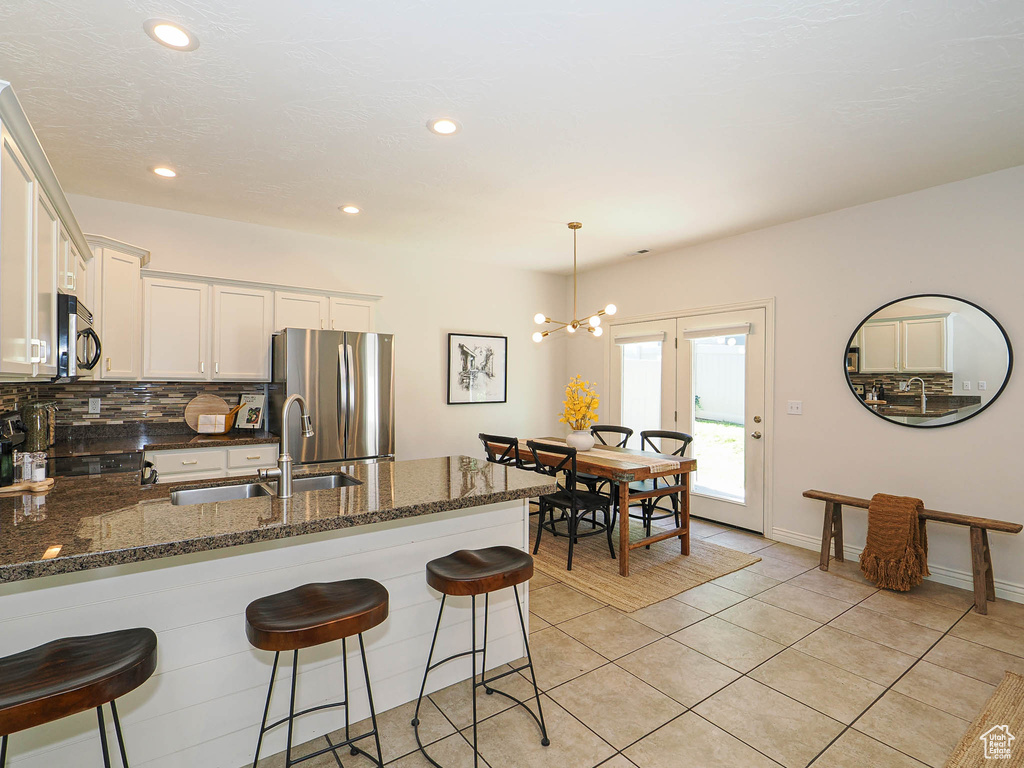 Kitchen featuring stainless steel appliances, a peninsula, white cabinets, light tile patterned flooring, and dark stone countertops