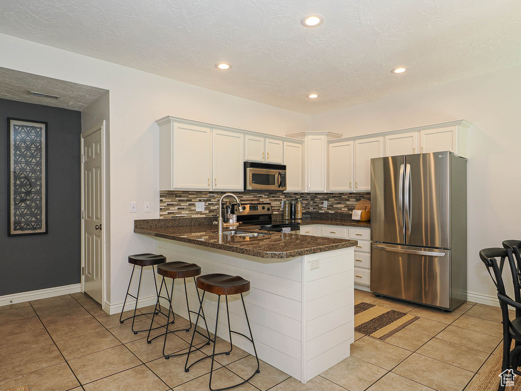 Kitchen with appliances with stainless steel finishes, a peninsula, light tile patterned floors, white cabinetry, and decorative backsplash