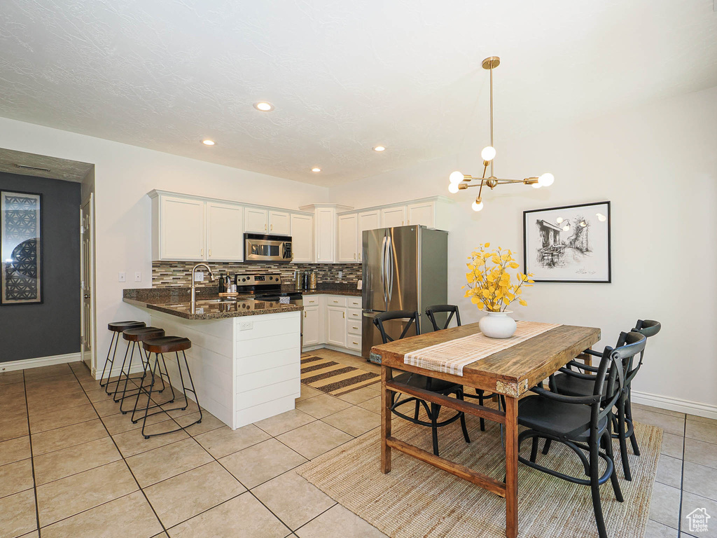 Kitchen featuring appliances with stainless steel finishes, a peninsula, light tile patterned floors, tasteful backsplash, and white cabinets