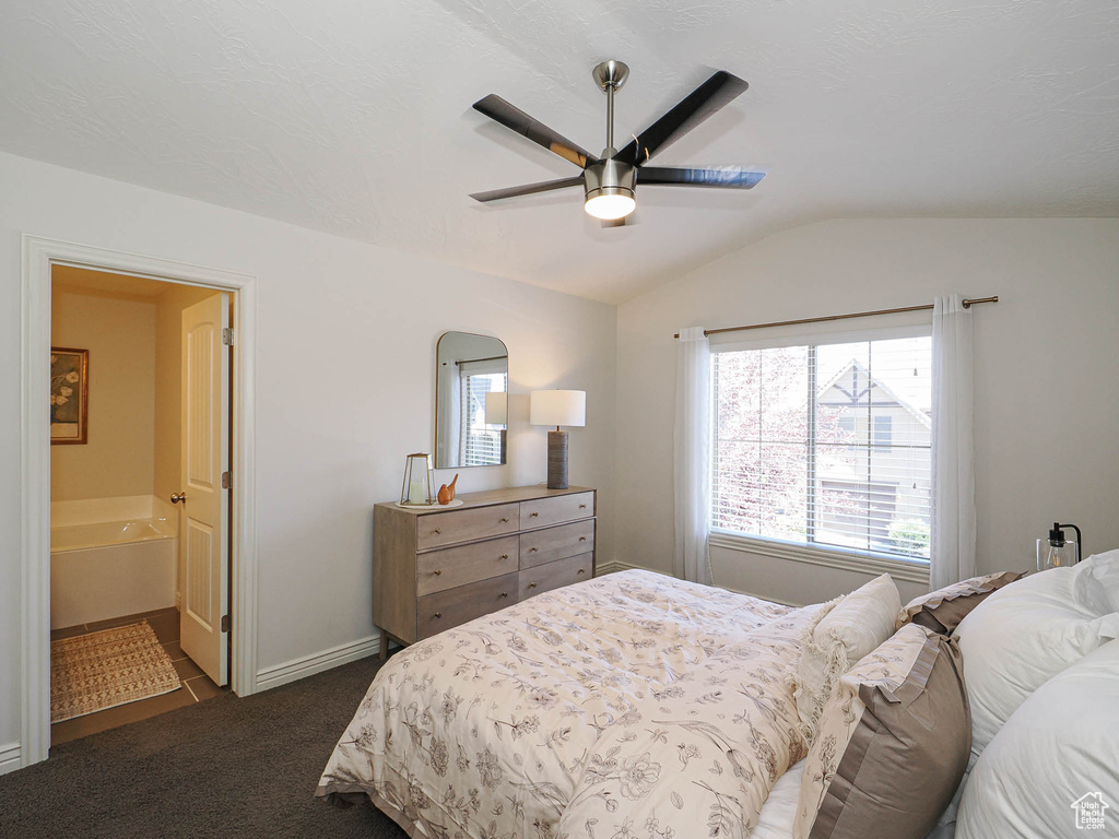 Bedroom featuring lofted ceiling, dark carpet, connected bathroom, and a ceiling fan