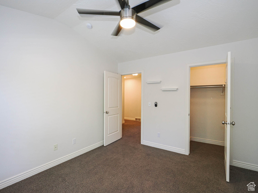 Unfurnished bedroom with dark carpet, a spacious closet, lofted ceiling, ceiling fan, and a closet