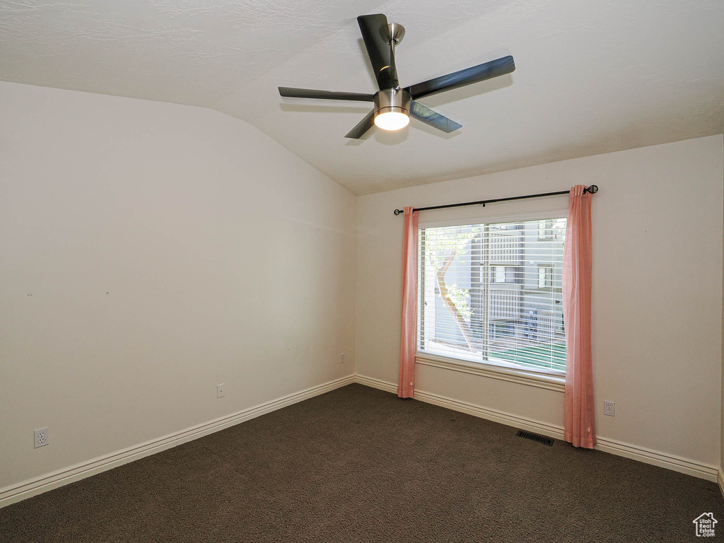 Spare room with vaulted ceiling, ceiling fan, and dark colored carpet