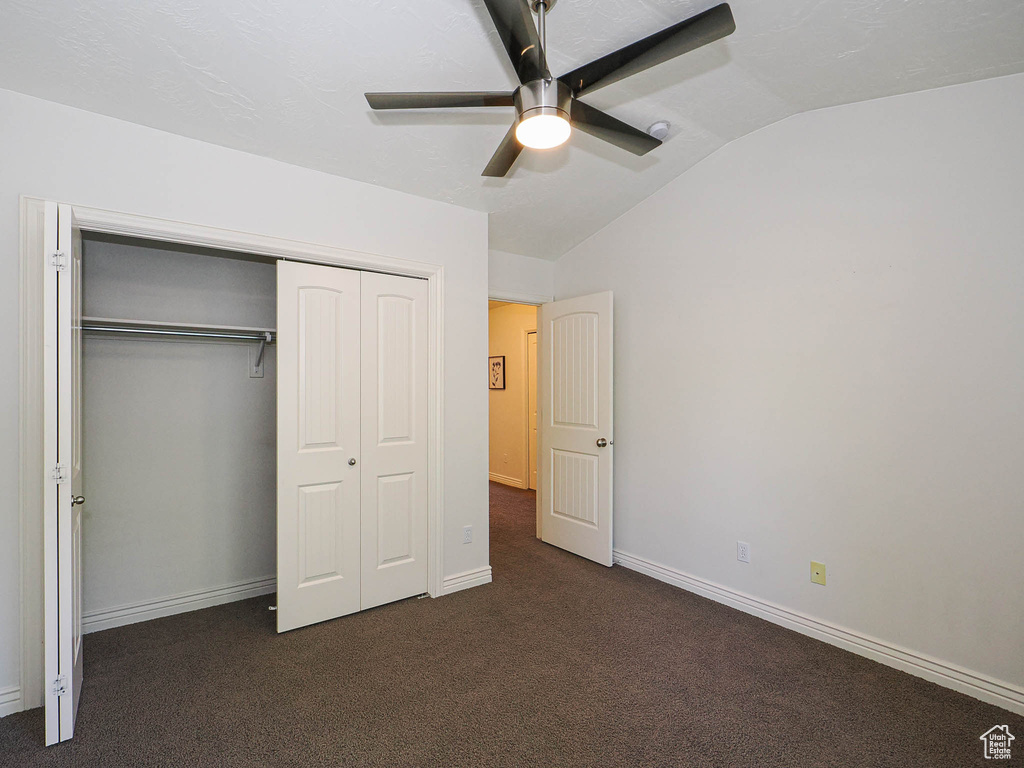 Unfurnished bedroom featuring vaulted ceiling, dark colored carpet, a closet, and ceiling fan