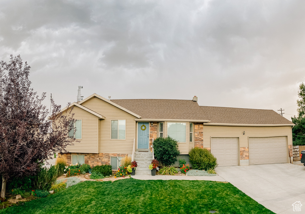 View of front facade with stone siding, an attached garage, concrete driveway, and a front yard