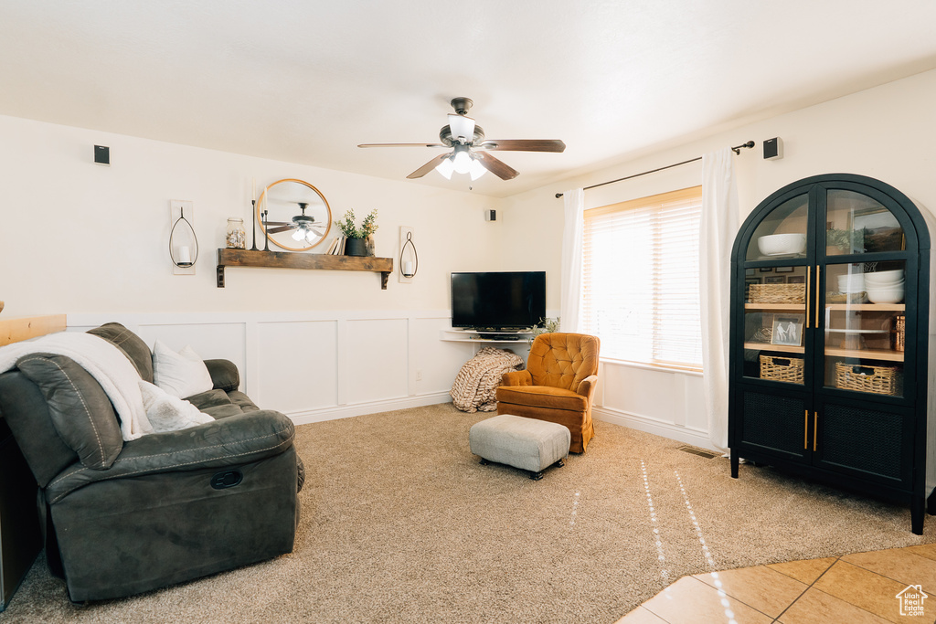 Living room with carpet, a ceiling fan, wainscoting, tile patterned floors, and a decorative wall
