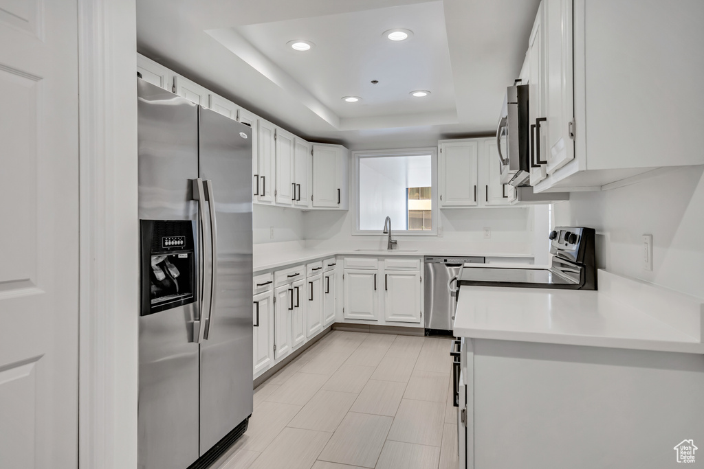 Kitchen with stainless steel appliances, recessed lighting, light countertops, white cabinets, and a raised ceiling