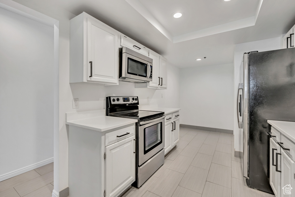 Kitchen featuring appliances with stainless steel finishes, recessed lighting, light countertops, white cabinets, and a tray ceiling