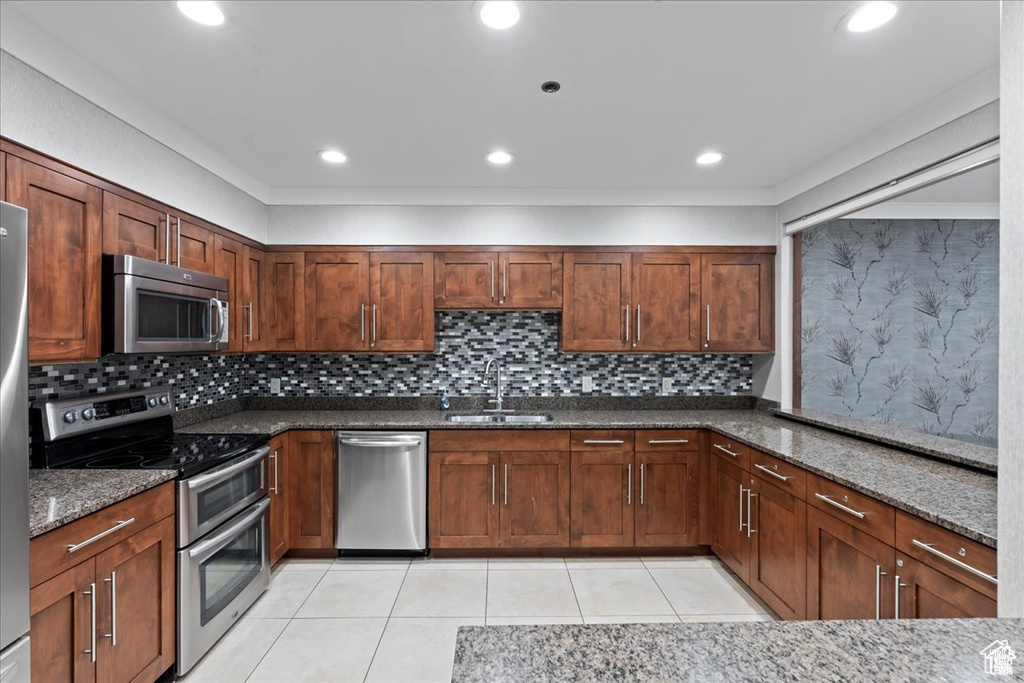 Kitchen featuring appliances with stainless steel finishes, dark stone countertops, light tile patterned floors, decorative backsplash, and recessed lighting