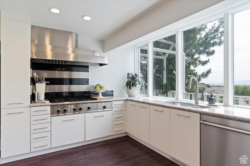 Kitchen with appliances with stainless steel finishes, wall chimney range hood, recessed lighting, light stone counters, and white cabinets