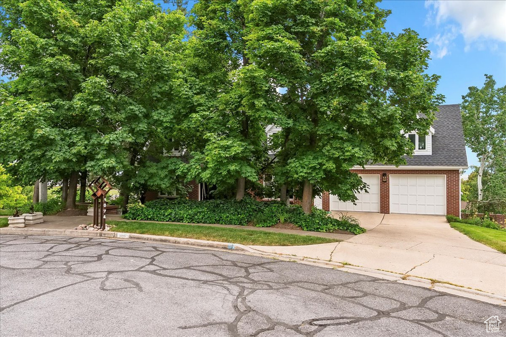Obstructed view of property with brick siding, driveway, an attached garage, and a shingled roof