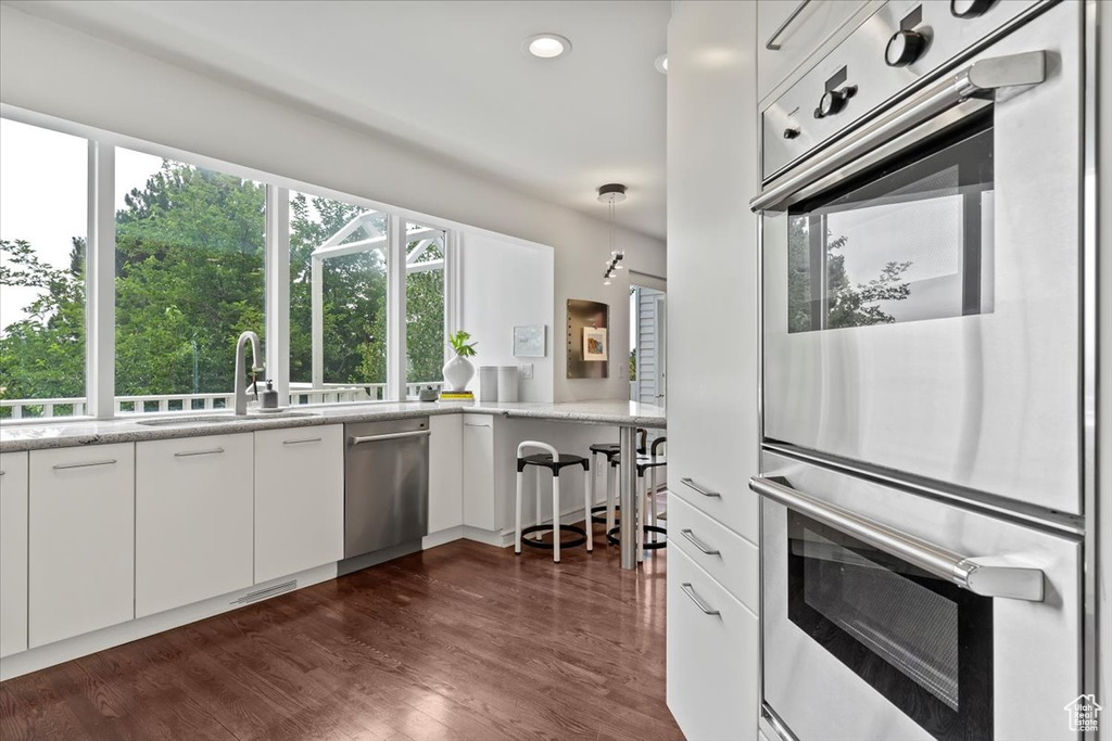 Kitchen featuring stainless steel appliances, white cabinets, dark wood finished floors, light stone counters, and recessed lighting