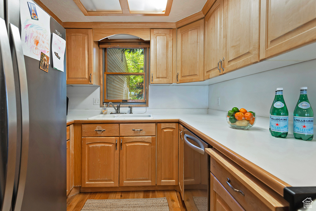 Kitchen with appliances with stainless steel finishes, light wood finished floors, and light countertops
