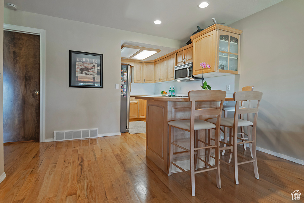 Kitchen featuring stainless steel appliances, light brown cabinets, a breakfast bar, light wood-style flooring, and recessed lighting