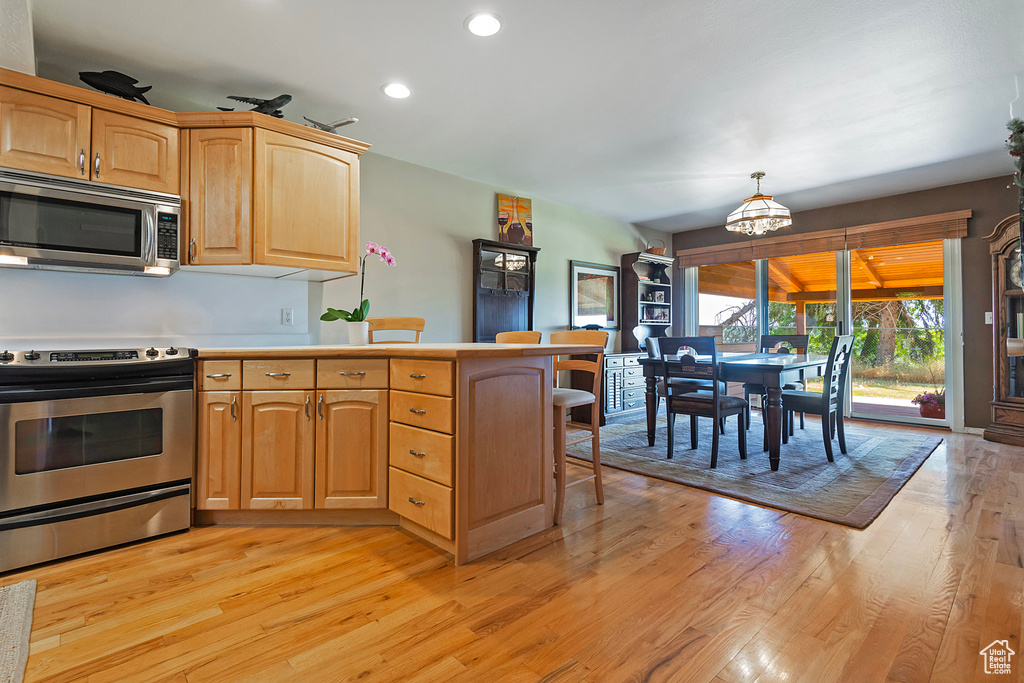 Kitchen featuring appliances with stainless steel finishes, a peninsula, light wood-style flooring, recessed lighting, and a chandelier