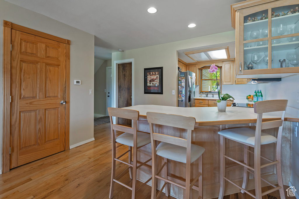 Kitchen with stainless steel fridge, light countertops, light wood finished floors, a kitchen bar, and recessed lighting