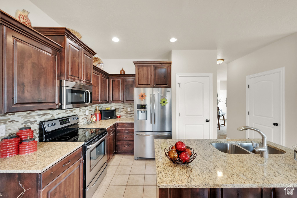 Kitchen with appliances with stainless steel finishes, light tile patterned floors, tasteful backsplash, light stone counters, and dark brown cabinetry
