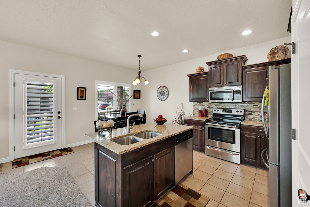 Kitchen with appliances with stainless steel finishes, light tile patterned floors, backsplash, an island with sink, and dark brown cabinetry
