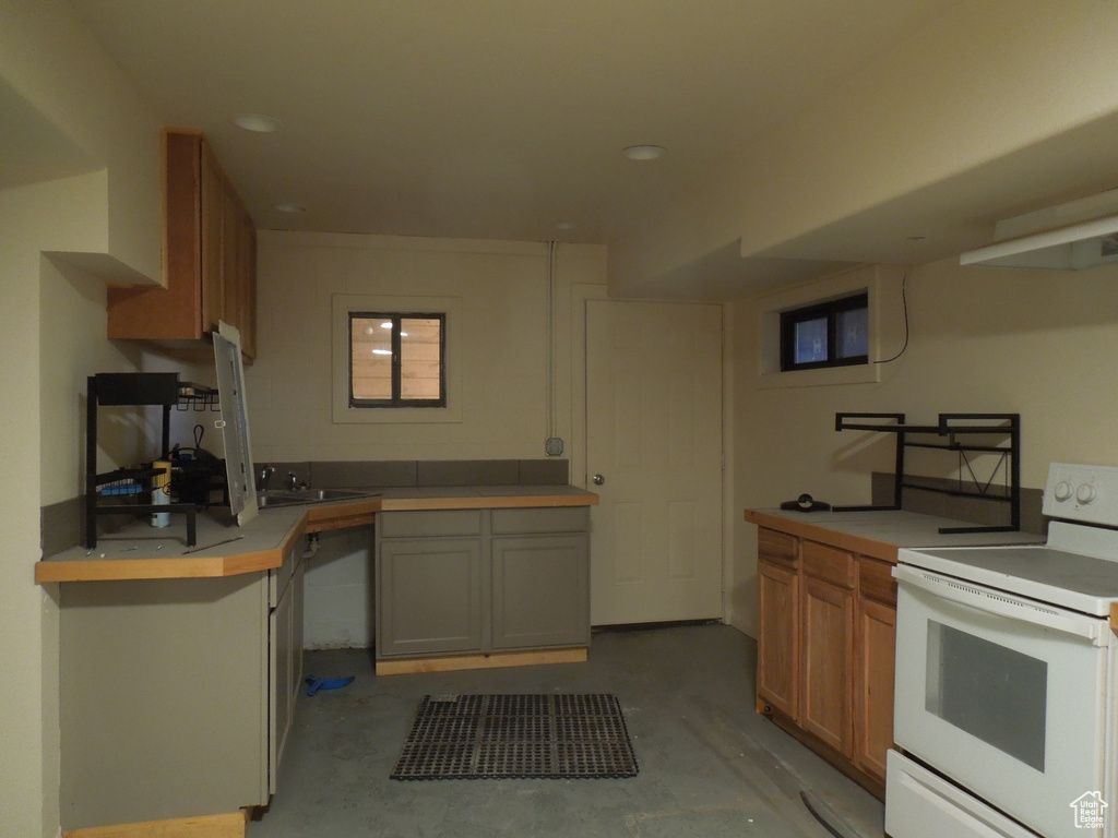 Kitchen with electric range, unfinished concrete floors, light countertops, brown cabinets, and recessed lighting