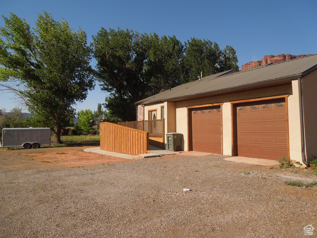 View of property exterior with stucco siding, a metal roof, dirt driveway, and a garage