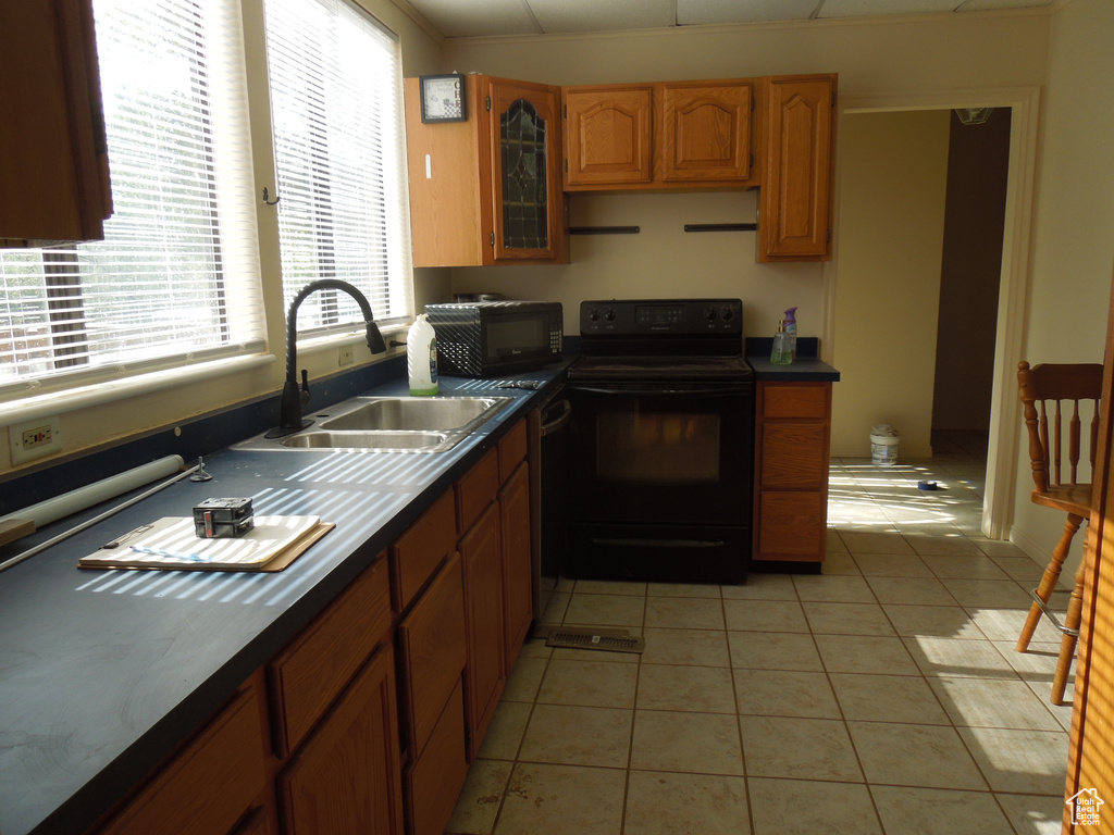 Kitchen featuring black appliances, light tile patterned flooring, dark countertops, and brown cabinets