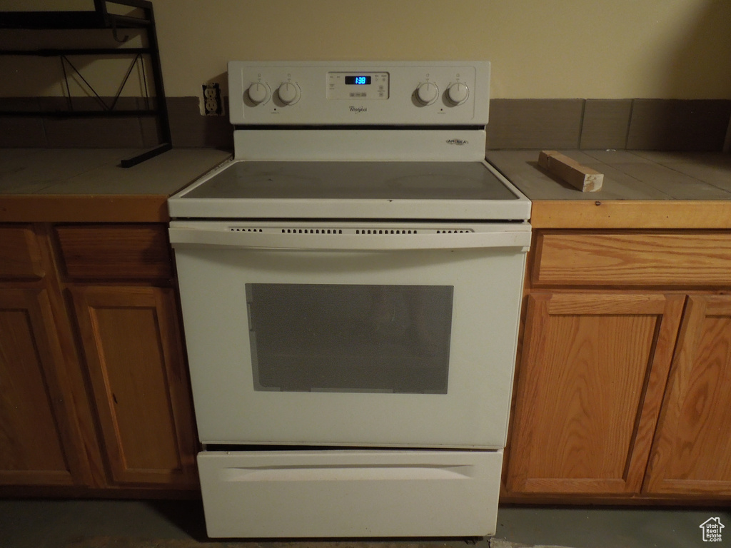 Kitchen with white range with electric stovetop, brown cabinets, and tile counters