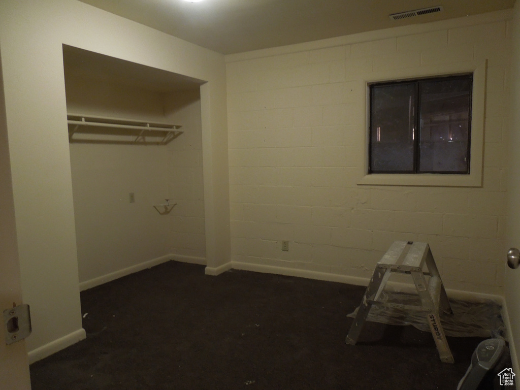 Unfurnished bedroom featuring dark carpet and concrete block wall