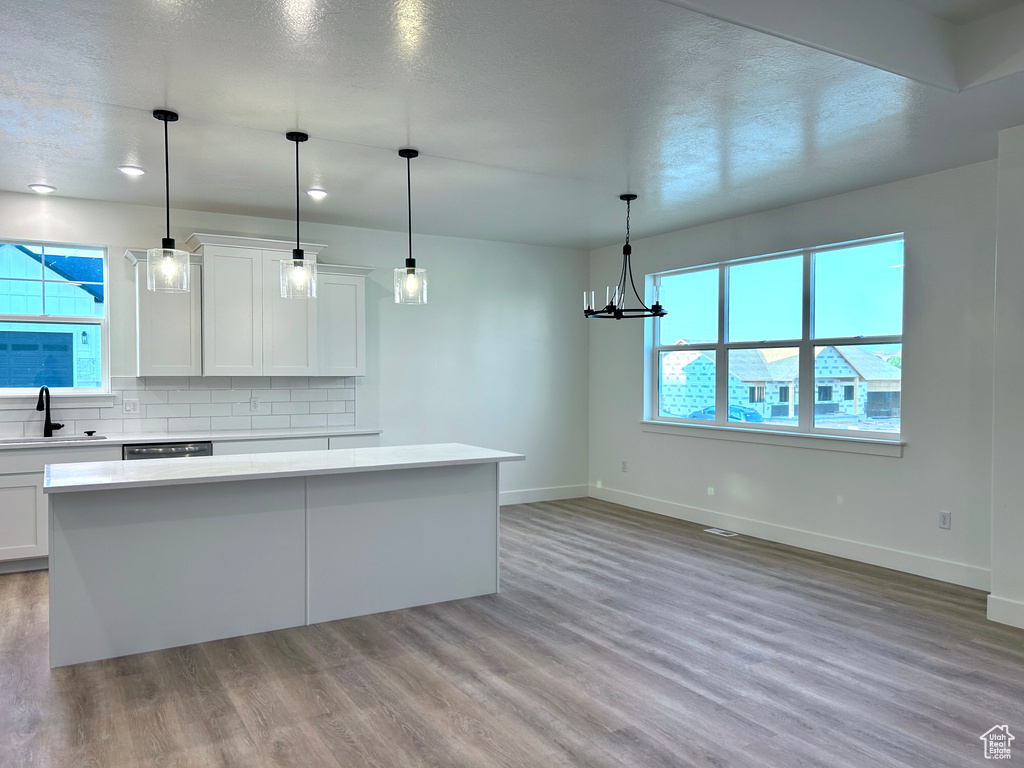 Kitchen featuring light wood-style floors, a center island, light countertops, backsplash, and white cabinetry