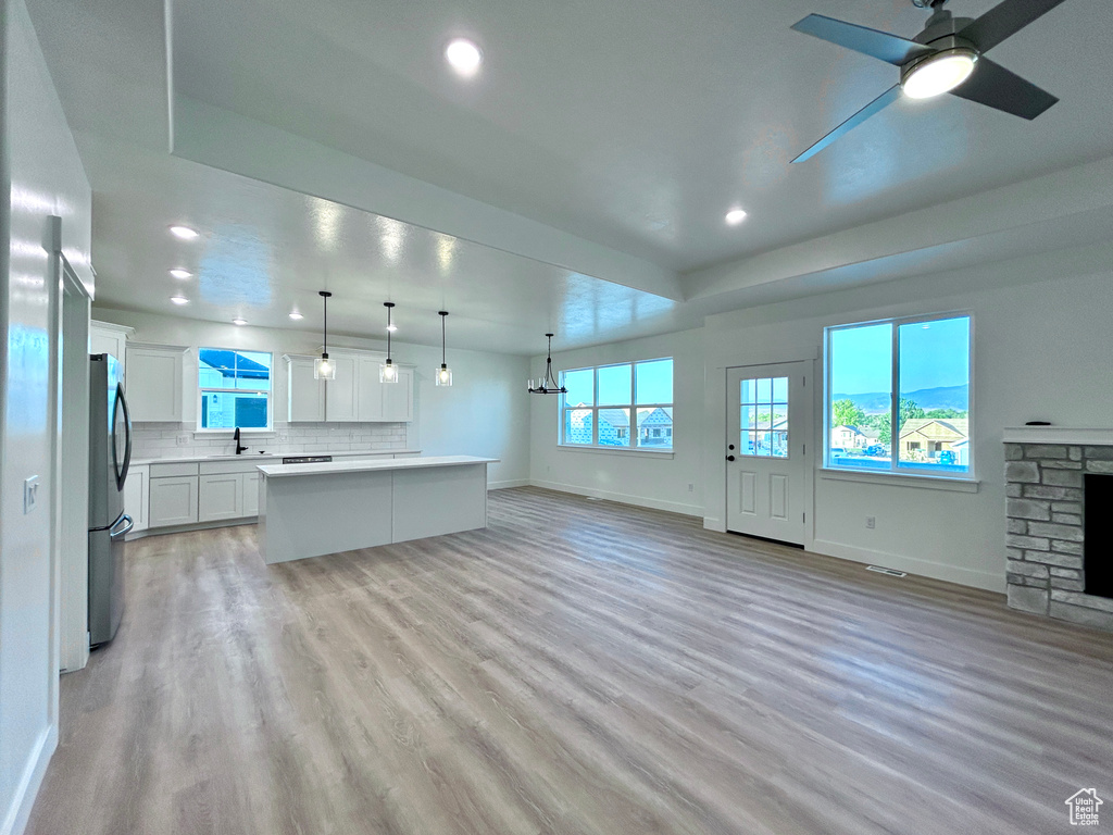 Unfurnished living room with plenty of natural light, recessed lighting, a stone fireplace, ceiling fan, and light wood-type flooring