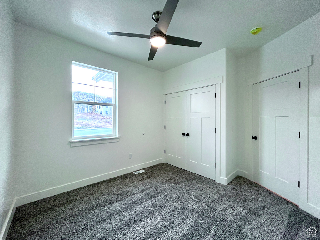 Unfurnished bedroom with dark colored carpet, a closet, and a ceiling fan