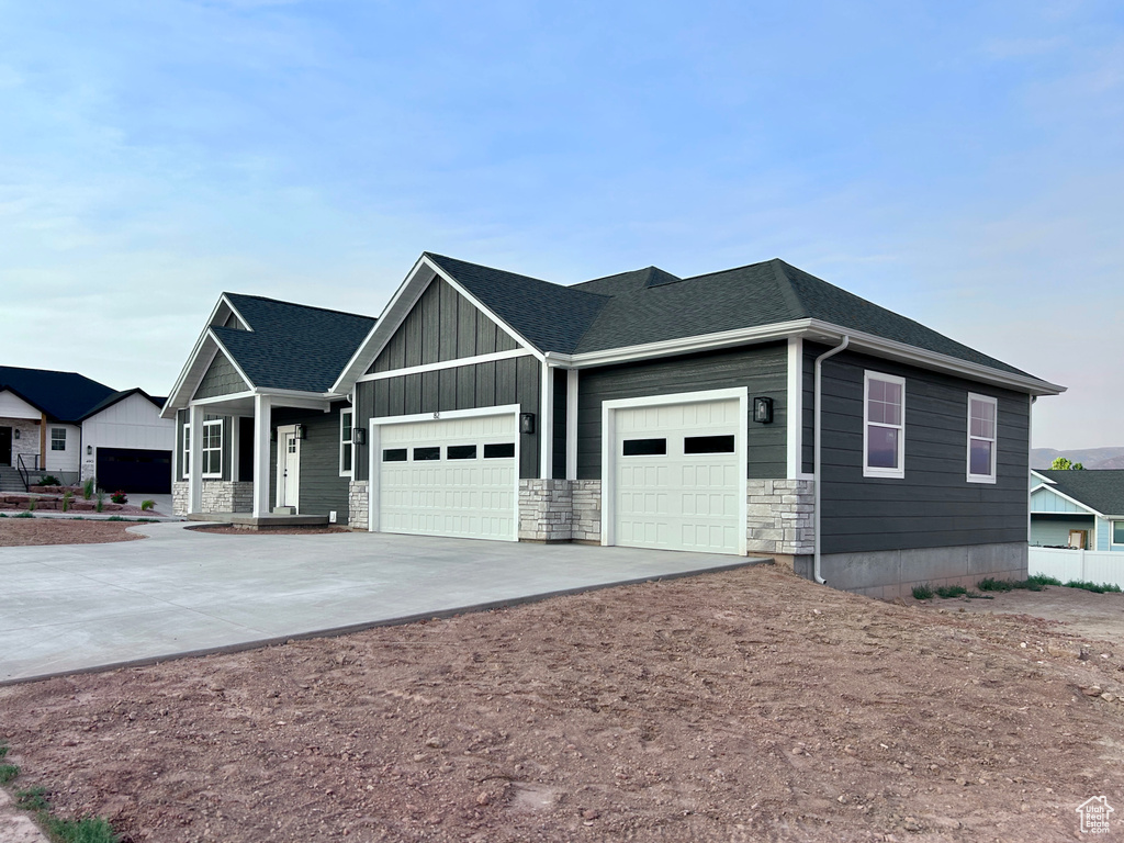 View of front of home with an attached garage, concrete driveway, board and batten siding, stone siding, and a shingled roof