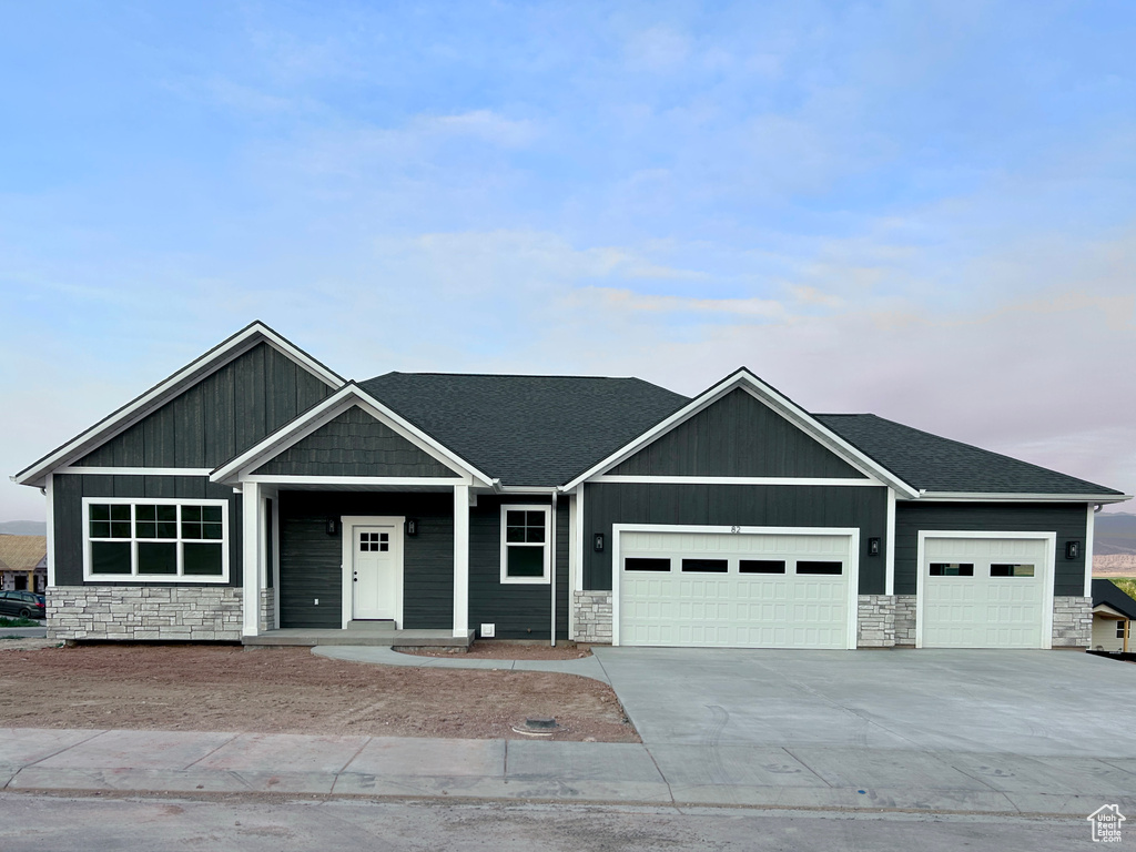 View of front facade with stone siding, a garage, concrete driveway, and a shingled roof