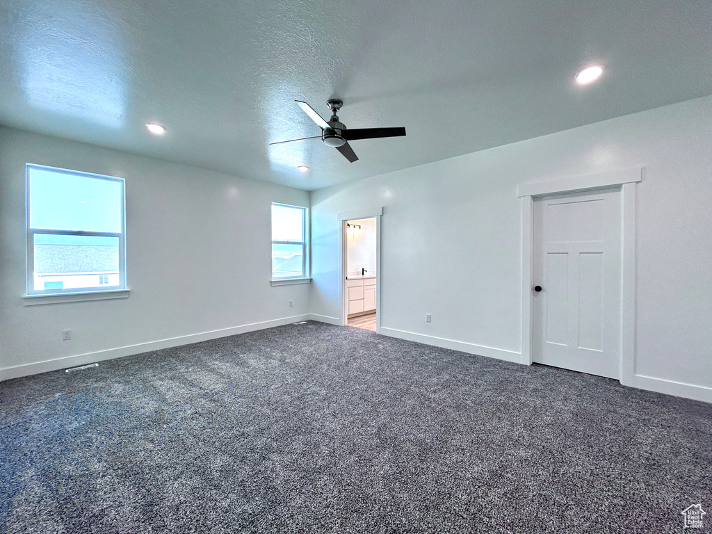 Unfurnished bedroom featuring multiple windows, dark carpet, recessed lighting, a ceiling fan, and connected bathroom